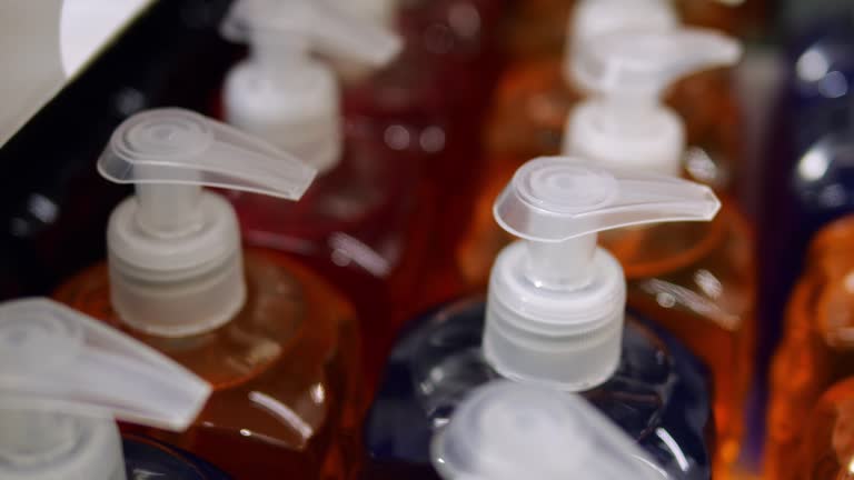 Rows unbranded transparent colorful bottles of consumer cosmetics with pumps. Unlabelled dark blue and orange shampoo or liquid soap in consumer packaging without logo.