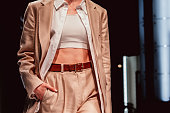 Fashion details of fancy stylish neutral beige outfit, classy jacket, crop top, pants with leather brown belt.