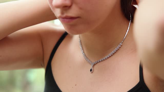 Unrecognizable woman put on a silver necklace with black gemstone