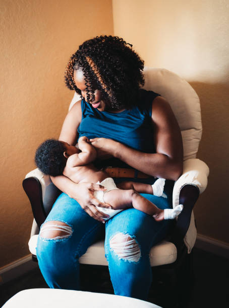 African American woman breastfeeds her 3 month old baby at home, motherhood stock photo