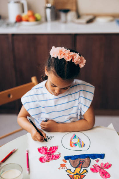 An adorable preschool Cuban child developing her creativity while standing at the table.