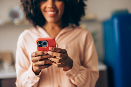 A close up view of an unrecognizable smiling Cuban entrepreneur texting on her smartphone while standing indoors.