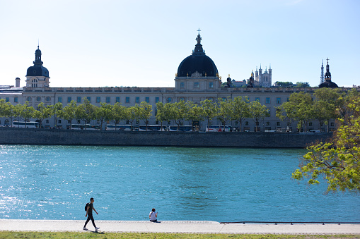 Lyon, France: A pedestrian walks along the Rhone River, with the 18th-century Hotel Dieu in the background. The building is now the luxury Intercontinental Hotel.