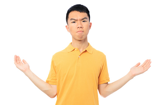 A teenage male Asian boy is confused and unsure, gesturing with his hands. He is frowning and looking at the camera. The background is white isolated. He is wearing a yellow golf shirt.