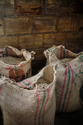 This image shows set of bags full of coffee in warehouse. Scene reveals neat stacking of heavy cloth or jute sacks, each filled to brim with dried coffee beans.