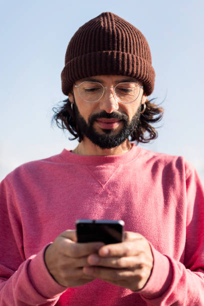 stylish bearded young man in pink jersey texting on his smart phone, concept of modern lifestyle and technology of communication
