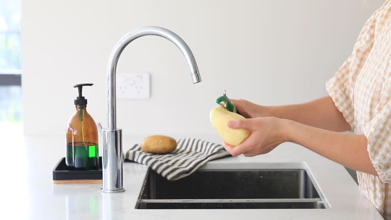 A woman peels potatoes with a vegetable peeler. The process of cooking a dish