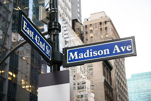 Madison Avenue and East 42nd Street steet signs in New York City. Buildings in background.