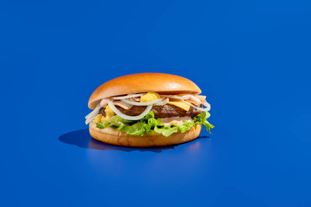 istock Tasty cheeseburger with onion, cheddar, sauce, and alternative meat on blue background. Modern, minimalist food photography, perfect for takeout. Horizontal composition, low-angle shot 1494440465