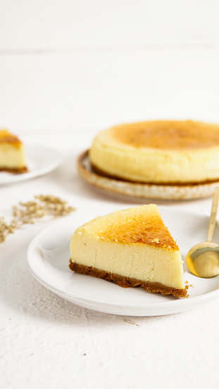 a slice of new york cheesecake, served on a dessert plate. The texture of the soft and dense cheese cake with the biscuit at the bottom is very appetizing, perfect for serving with a cup of coffee.