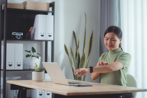 Asian woman suffering from irritate dry skin and scratching her skin sitting at home office.