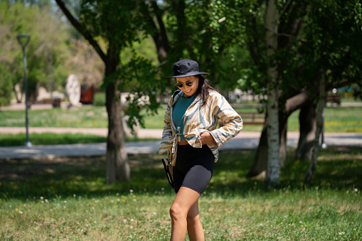 The general plan of a young woman, Asian (Kazakh) in sunglasses and a hat. A happy girl of oriental appearance walks in a summer park.