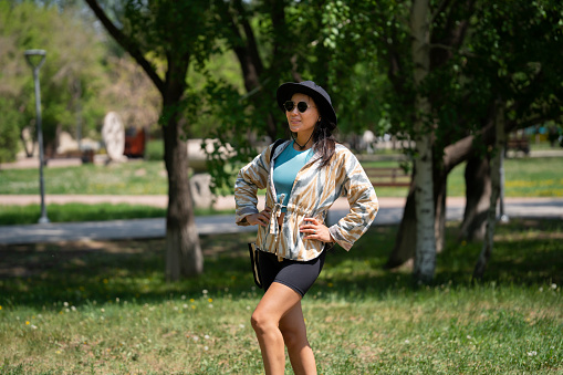 The general plan of a young woman, Asian (Kazakh) in sunglasses and a hat. A happy girl of oriental appearance walks in a summer park.