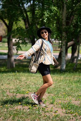 The general plan of a young woman, Asian (Kazakh) in sunglasses and a hat. A happy girl of oriental appearance walks in a summer park.