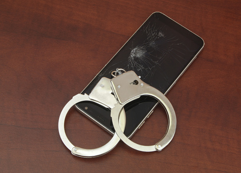 Broken mobile phone and handcuffs on table close-up.