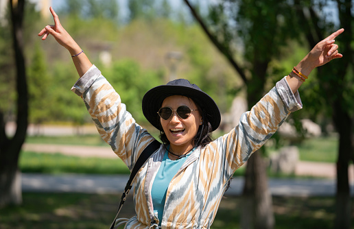 The general plan of a young woman, Asian (Kazakh) in sunglasses and a hat. A happy girl of oriental appearance walks in a summer park.