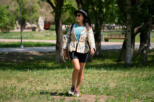 The general plan of a young woman, Asian (Kazakh) in sunglasses and a hat. A happy girl of oriental appearance walks in a summer park.