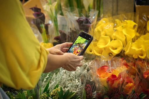 An Asian woman is taking a photo of the flowers in front of her with her mobile phone