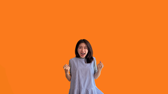 Asian woman posing extremely happy to win, Successful, Show extreme happiness, Very happy, yes, Lonely woman on orange background.
