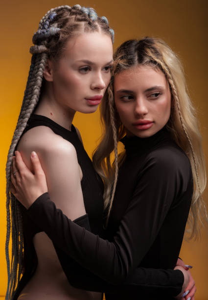 istock Two girlfriend hugging each other, feeling love, posing in black bodysuit with long hair, perfect lips and skin, looking in camera on warm orange background. 1494479353