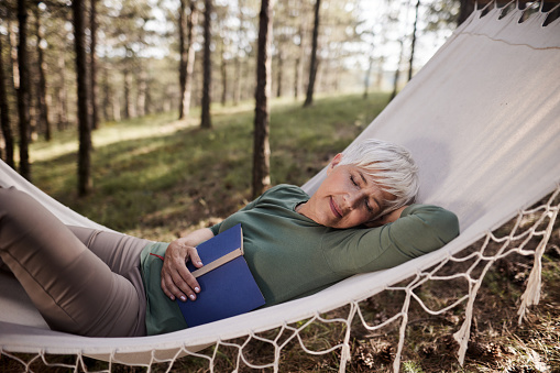 Relaxed mature woman enjoying while taking a nap in hammock outdoors.