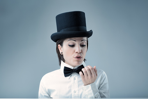 Woman in top hat, air of superiority, blowing on her nails, demands nothing less than her standards. White shirt, black bow tie, neutral background