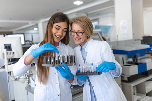 Two scientists are working in laboratory. Young female researcher and her senior supervisor are doing investigations with test tubes.