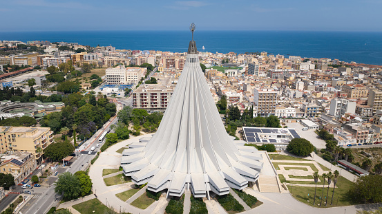 Madonna delle Lacrime Basilica (Our Lady of the Tears), also called Madonnina delle Lacrime roman catholic church in the city center of Siracusa - Syracuse in Sicily. Construction started in the year 1966, the first stone for construction was consecrated in 1954. Aerial Drone Point of View Cityscape Stitched Panorama towards the Mediterranean Coast. Syracuse, Sicily Island, Italy, Southern Europe