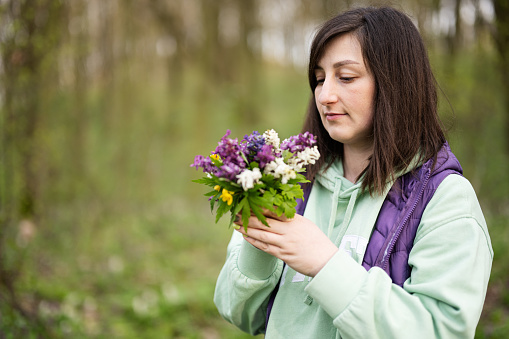 Portrait of woman with spring bouquet of flowers on forest. Outdoor leisure concept.