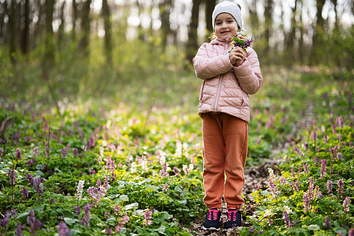 Portrait little girl with bouquet of flowers on sunny forest. Outdoor spring leisure concept.