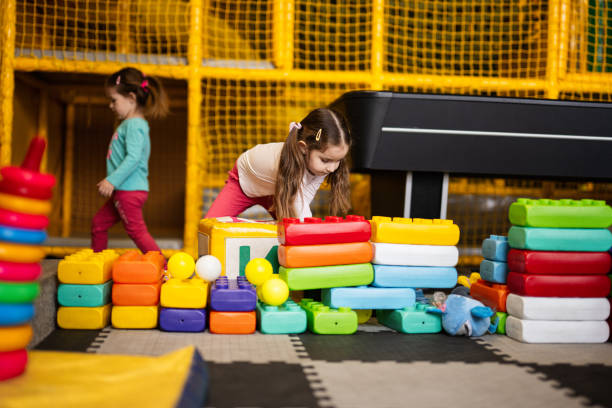 Two sisters playing at kids play center while build with colored plastic blocks.