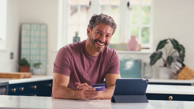 Portrait Of Mature Man With Credit Card Using Digital Tablet At Home To Book Holiday Or Shop