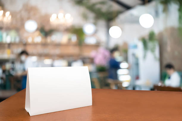 Blank menu frame label mockup. Mock up menu frame on table in bar restaurant, stand for booklet with white sheet of acrylic tent card paper in blur cafeteria Blank menu frame label mockup. Mock up menu frame on table in bar restaurant, stand for booklet with white sheet of acrylic tent card paper in blur cafeteria, cook chef in background. restaurant table card stock pictures, royalty-free photos & images