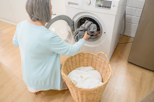 happy senior household, the mother, a beautiful senior woman, takes care of the laundry using a washing machine. It's a routine part of their lifestyle to keep their home clean and organized