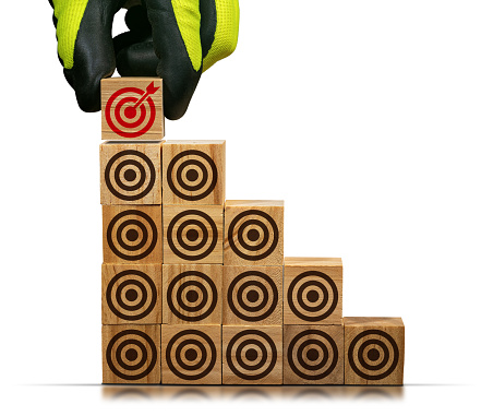 Gloved hand arranging wood blocks with many empty brown targets and one red one with an arrow reaching into the center, isolated on white background.