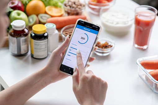 Woman professional nutritionist working and checking data from a smartphone with a variety of fruits, nuts, vegetables, and dietary supplements on the table