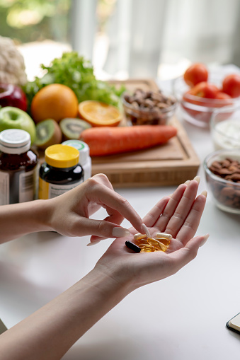 Woman professional nutritionist checking dietary supplements in hand, surrounded by a variety of fruits, nuts, vegetables, and dietary supplements on the table
