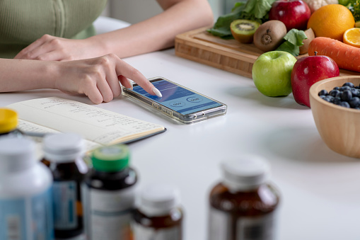 Woman professional nutritionist working and checking data from a smartphone with a variety of fruits, nuts, vegetables, and dietary supplements on the table