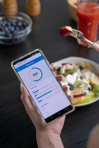 Photo of Woman checking calories and nutrients app on her phone while having a meal