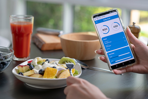 Woman checking calories and nutrients app on her phone while having a meal. Professional Nutritionist.