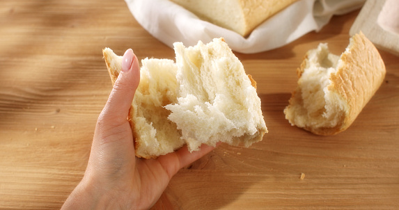 Female hands tear fresh bread. Texture of bread close up. Wooden background. Slow mation. Sunny day. First person view.