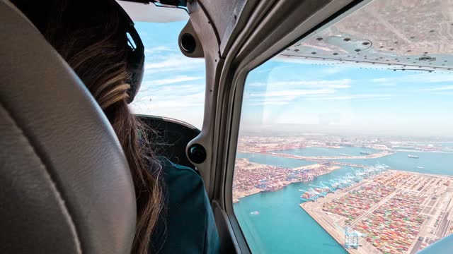 A young female pilot is piloting the airplane flying over the harbor