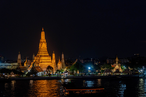 Beautiful view on Wat Arun by night with a illuminated boat on the river, from a sunset footop bar in Bangkok, Thailand