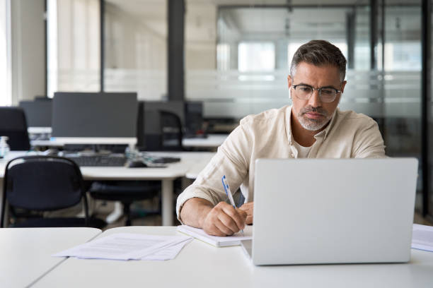 istock Focused mature Latin businessman working on laptop in office with copy space. 1494498480