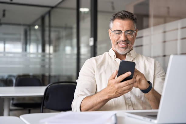 istock Middle aged Hispanic manager ceo businessman using cell phone mobile app, laptop 1494498494