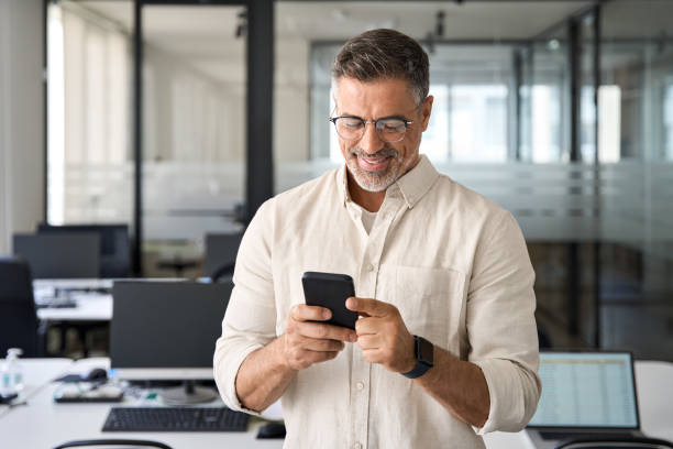 istock Smiling mature businessman holding and using smartphone applications in office. 1494498503