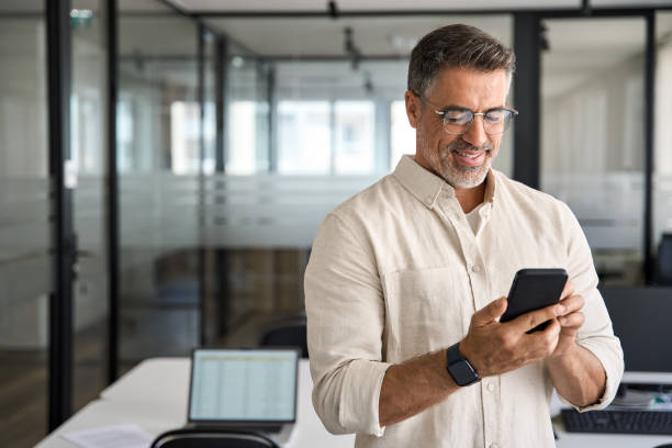 istock Smiling mature businessman holding and using smartphone applications in office. 1494498510