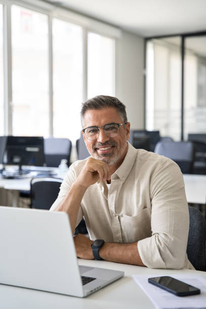 オフィスで成熟したインド人またはラテン人の笑顔のビジネスマンの職場でのポートレート。 - male senior adult men portrait ストックフォトと画像