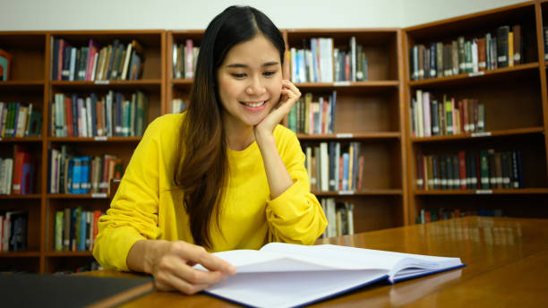 istock Pleased female student reading book in a library for studying and research. Education, learning, knowledge and university. 1494498721