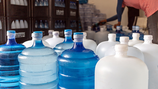 Plastic big bottles or white and blue gallons of purified drinking water inside the production line to prepare for sale. Water drink factory, small business